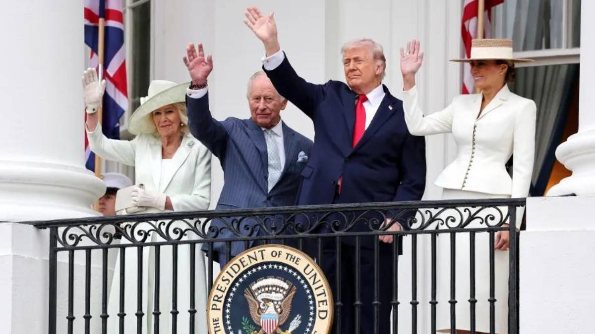 Four people in formal attire on a white balcony, waving to a crowd, with the presidential seal visible on the railing.