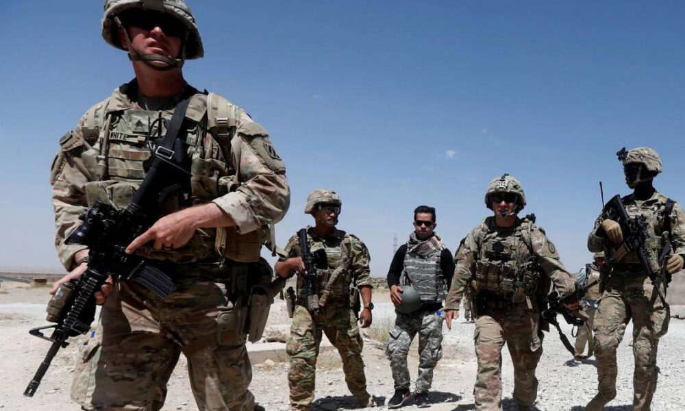 Group of soldiers in desert camouflage marching toward the camera, armed with rifles and wearing body armor under a clear blue sky.
