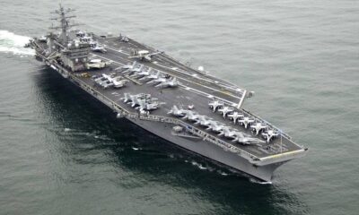 Military aircraft carrier at sea with multiple fighter jets lined up on deck and crew areas visible on the flight deckwise.
