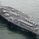 Military aircraft carrier at sea with multiple fighter jets lined up on deck and crew areas visible on the flight deckwise.