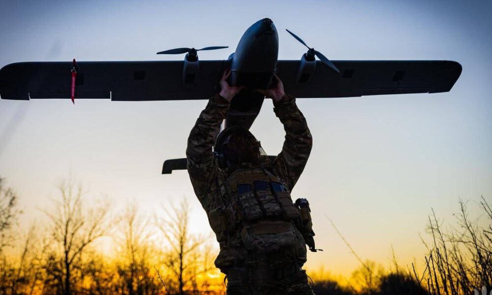 Soldier in camouflage gear lifts a small propeller plane overhead at sunset.