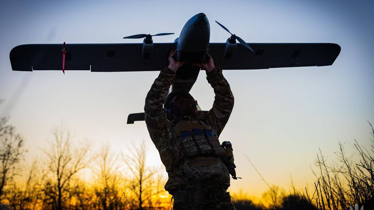 Soldier in camouflage gear lifts a small propeller plane overhead at sunset.