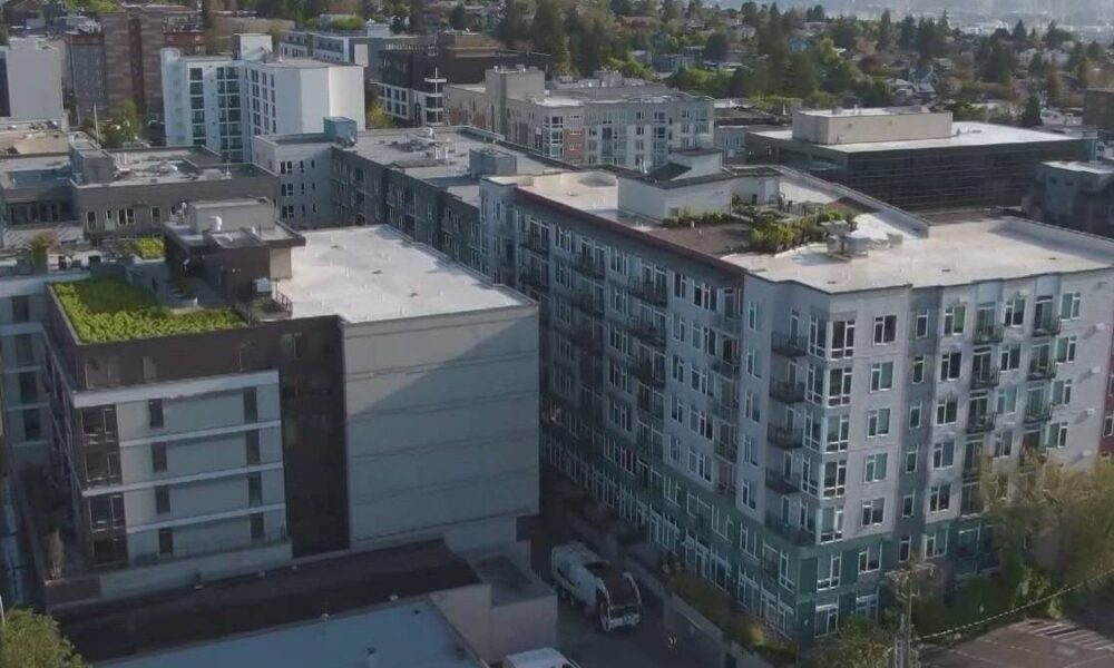 Aerial view of a modern multi-story apartment complex in a city neighborhood, with balconies and flat roofs seen from above.