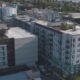 Aerial view of a modern multi-story apartment complex in a city neighborhood, with balconies and flat roofs seen from above.