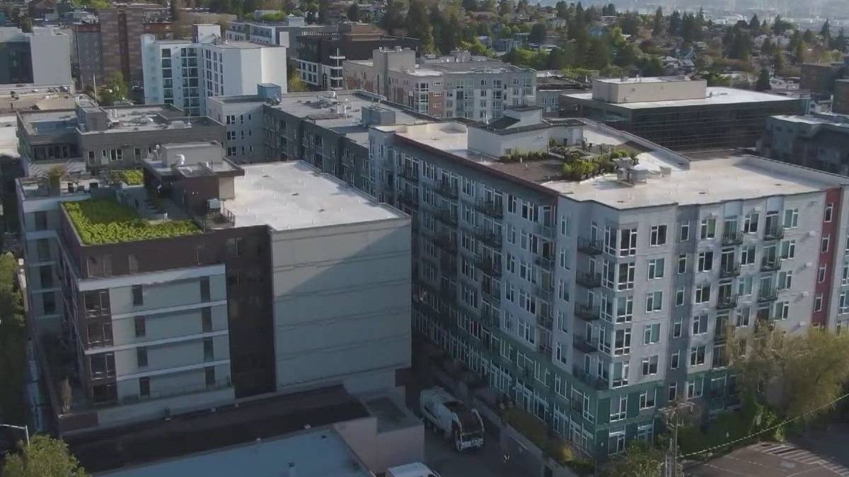 Aerial view of a modern multi-story apartment complex in a city neighborhood, with balconies and flat roofs seen from above.