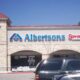 Albertsons storefront with blue sign and Savon Pharmacy to the right, brick building and cars in a shopping center parking lot under a clear blue sky