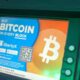 Bitcoin ATM screen advertising Bitcoin purchase with a large Bitcoin logo and colorful display.