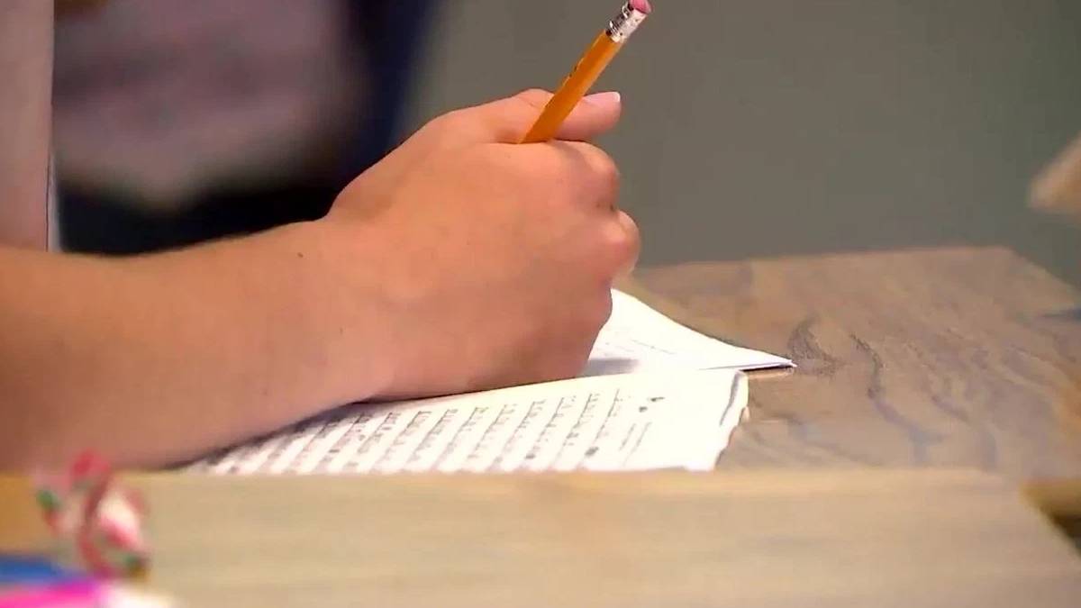 Close-up of a hand writing with a yellow pencil on lined paper at a wooden desk.