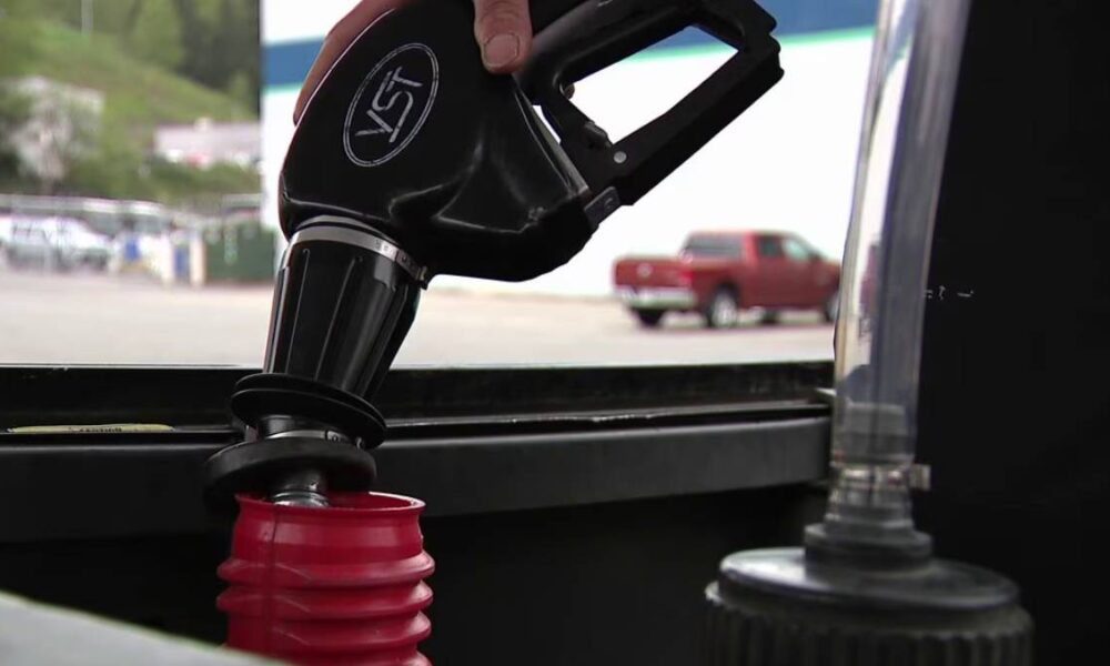 Close-up of a fuel nozzle being inserted into a car's fuel tank at a gas station.