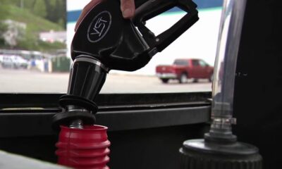 Close-up of a fuel nozzle being inserted into a car's fuel tank at a gas station.