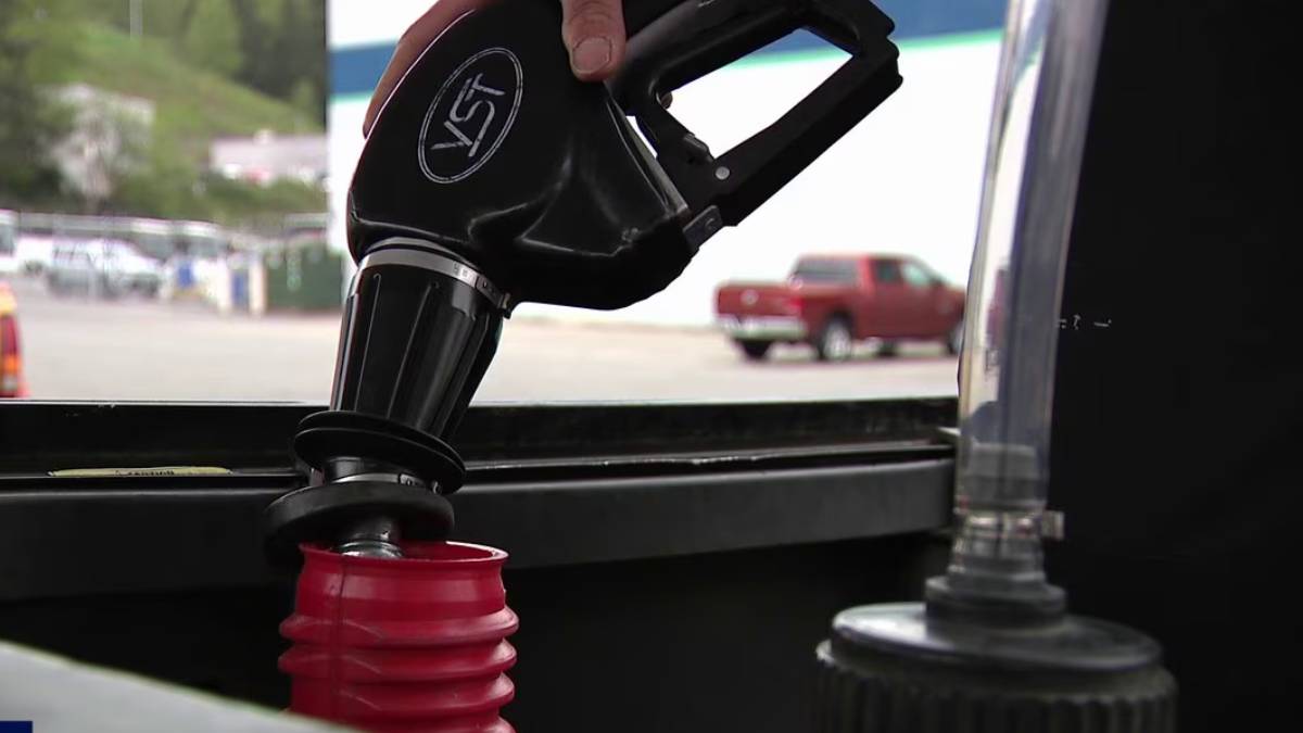 Close-up of a fuel nozzle being inserted into a car's fuel tank at a gas station.