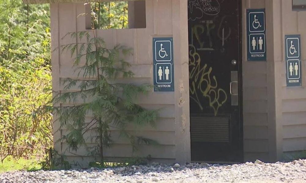 Exterior restroom building with multiple wheelchair-accessible signs on the walls and graffiti visible inside the doorway.