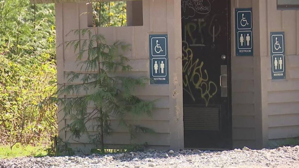 Exterior restroom building with multiple wheelchair-accessible signs on the walls and graffiti visible inside the doorway.