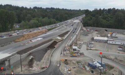 Aerial view of a large highway construction site with an elevated road, dirt piles, and heavy machinery nearby.