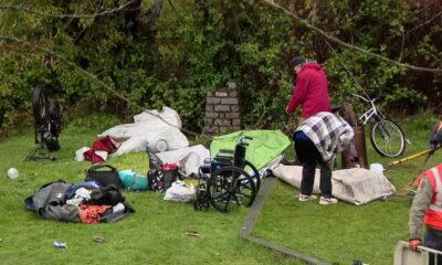 Outdoor cleanup scene: scattered gear, clothing, and tents on the grass with a wheelchair and a bicycle nearby.