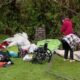 Outdoor cleanup scene: scattered gear, clothing, and tents on the grass with a wheelchair and a bicycle nearby.