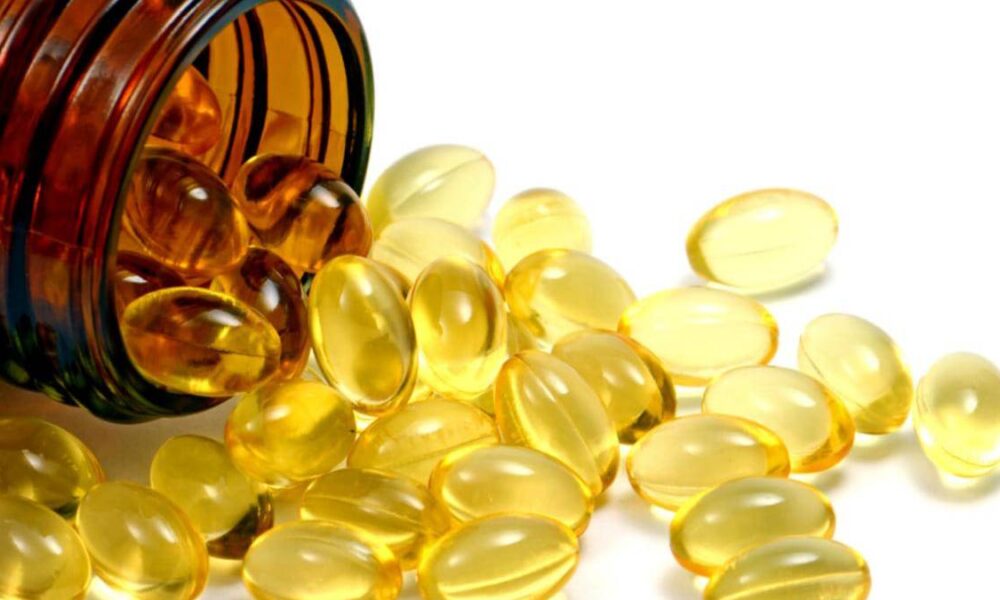 Brown glass bottle tipped over, spilling yellow softgel capsules onto a white surface.