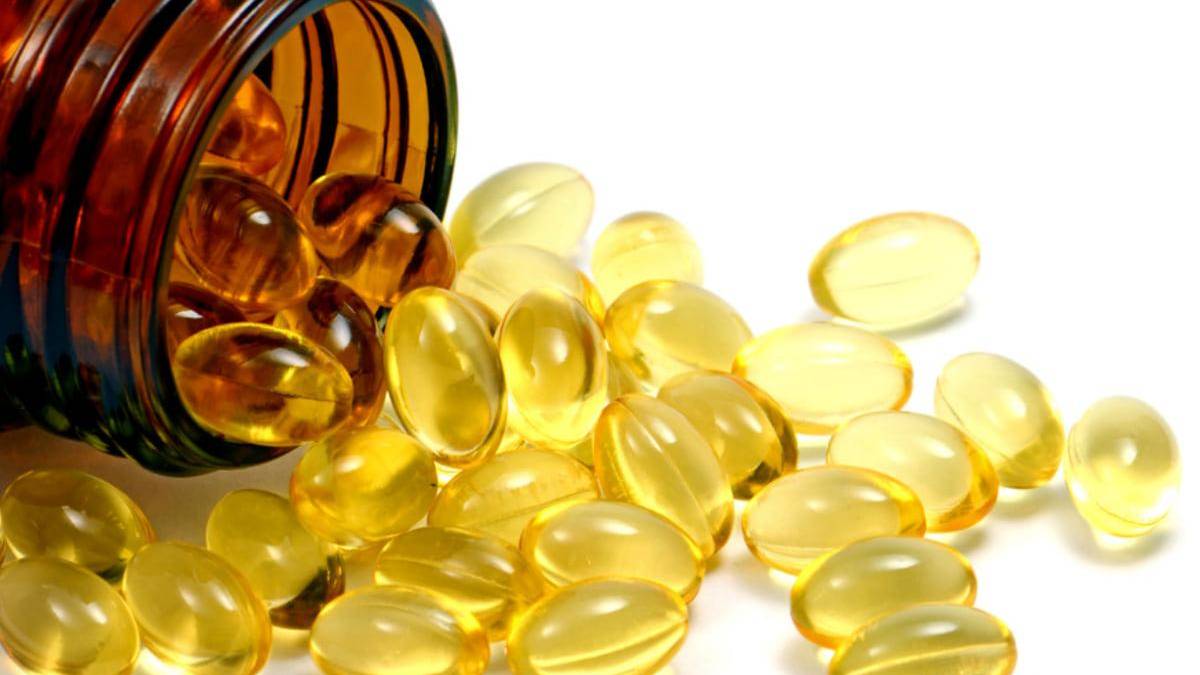 Brown glass bottle tipped over, spilling yellow softgel capsules onto a white surface.