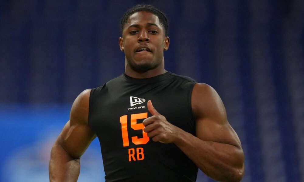 Athlete wearing a black sleeveless jersey with orange number 15 and RB, running on a field indoors.