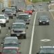 Heavy traffic on a multi-lane highway with many cars in the left lanes and a construction zone on the right shoulder barrier.
