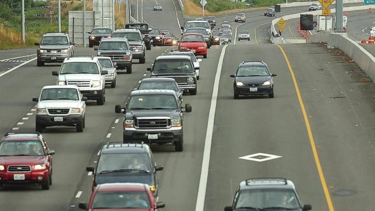Heavy traffic on a multi-lane highway with many cars in the left lanes and a construction zone on the right shoulder barrier.