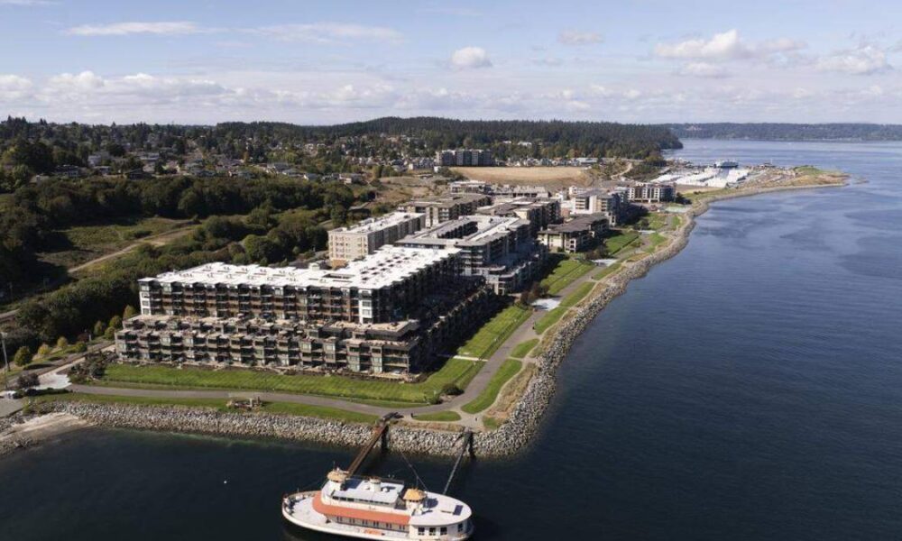 Aerial view of a large coastal residential complex with multi-story buildings along a rocky shoreline and a docked boat at the pier.