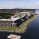 Aerial view of a large coastal residential complex with multi-story buildings along a rocky shoreline and a docked boat at the pier.