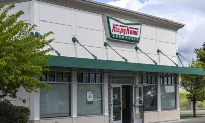 Krispy Kreme Doughnuts storefront with a green awning and the logo above the entrance. The windows show a closed sign/blank interior nearby.