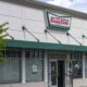Krispy Kreme Doughnuts storefront with a green awning and the logo above the entrance. The windows show a closed sign/blank interior nearby.