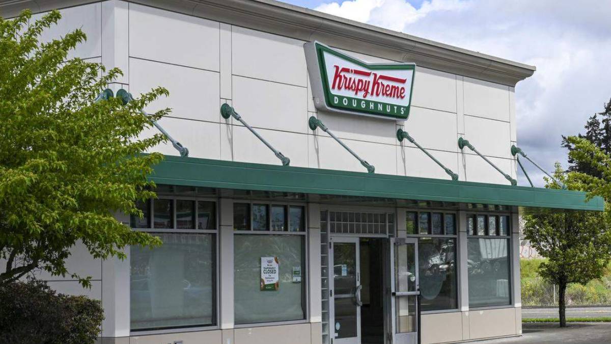 Krispy Kreme Doughnuts storefront with a green awning and the logo above the entrance. The windows show a closed sign/blank interior nearby.