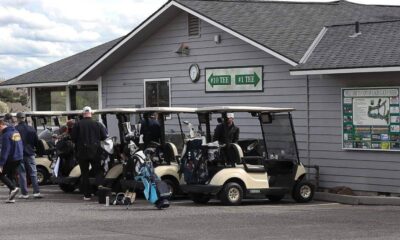 Golf carts lined up outside a golf club with players and bags ready to play. Sign shows #10 and #1 tees on the building.
