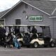 Golf carts lined up outside a golf club with players and bags ready to play. Sign shows #10 and #1 tees on the building.