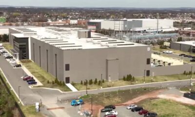 Aerial view of a large gray industrial building complex with a 'B' on the side, parking lots, and surrounding roads.