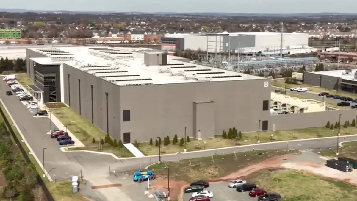 Aerial view of a large gray industrial building complex with a 'B' on the side, parking lots, and surrounding roads.