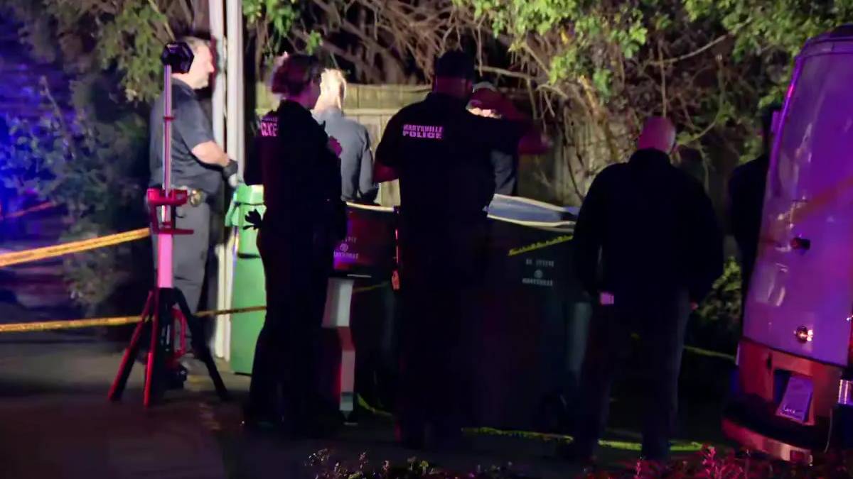 Nighttime crime scene with multiple investigators and police, yellow caution tape, and a van nearby under blue and purple lights.