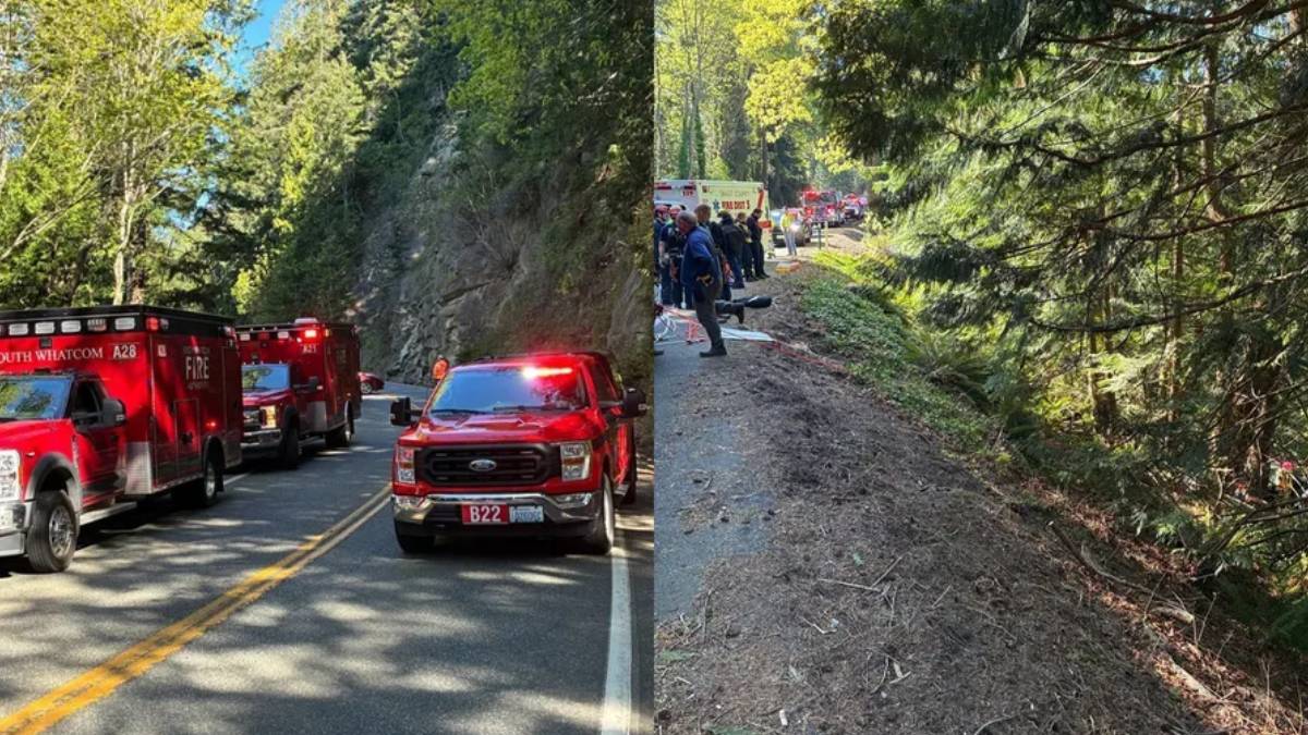 Emergency response on a rural road with red fire trucks and flashing lights blocking the lane; forested hillside in the background.