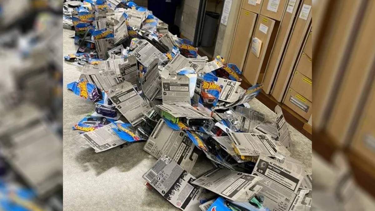 Pile of opened Hot Wheels packaging scattered on a concrete floor in a storage room, with tall cardboard boxes in the background.