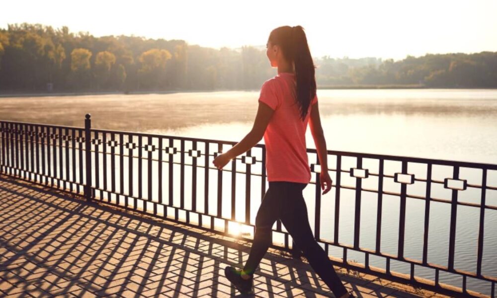 Woman walking along a railing by a lake at sunset on a sunny day.