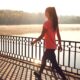 Woman walking along a railing by a lake at sunset on a sunny day.