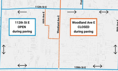 Map showing roads open for paving on 112th St E (left) with blue border; Woodland Ave E closed during paving on the right (orange border). 112th St E at top, 128th St E at bottom, Canyon Rd E left, 86th Ave E right; arrows show travel directions.