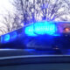 Police car roof with flashing blue emergency lights, evening scene with bare trees in background