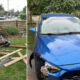 Split image: left shows a damaged wooden fence with scattered boards in a yard; right shows a blue car with front-end damage and missing bumper part on the driveway.
