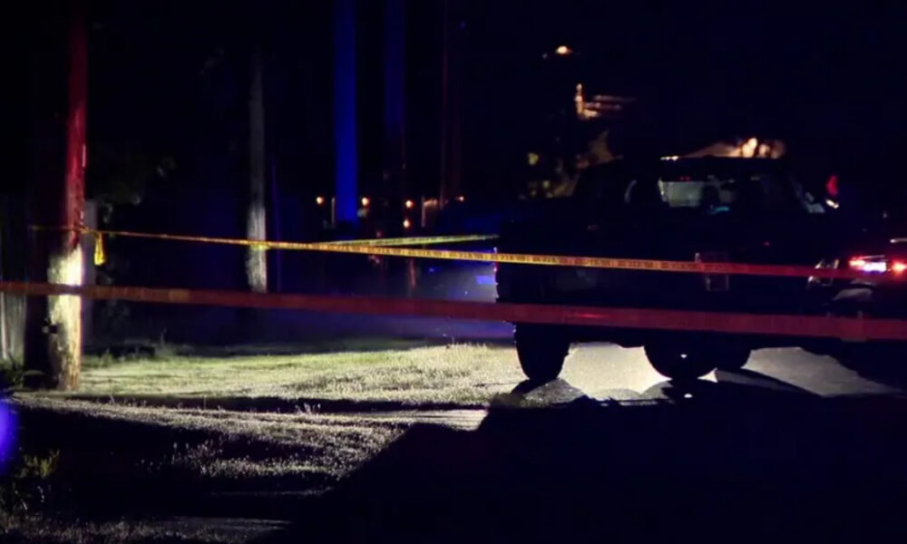 Night scene at a crime scene: yellow caution tape blocks a street with a dark SUV and faint emergency lights in the background.