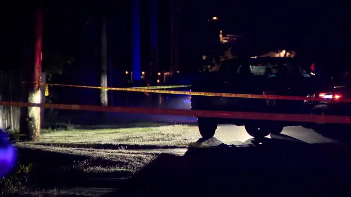 Night scene at a crime scene: yellow caution tape blocks a street with a dark SUV and faint emergency lights in the background.