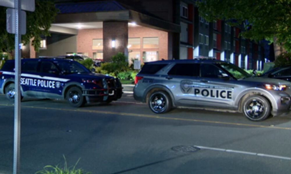 Two police SUVs parked on a city street at night; one shows Seattle Police lettering, the other reads POLICE.