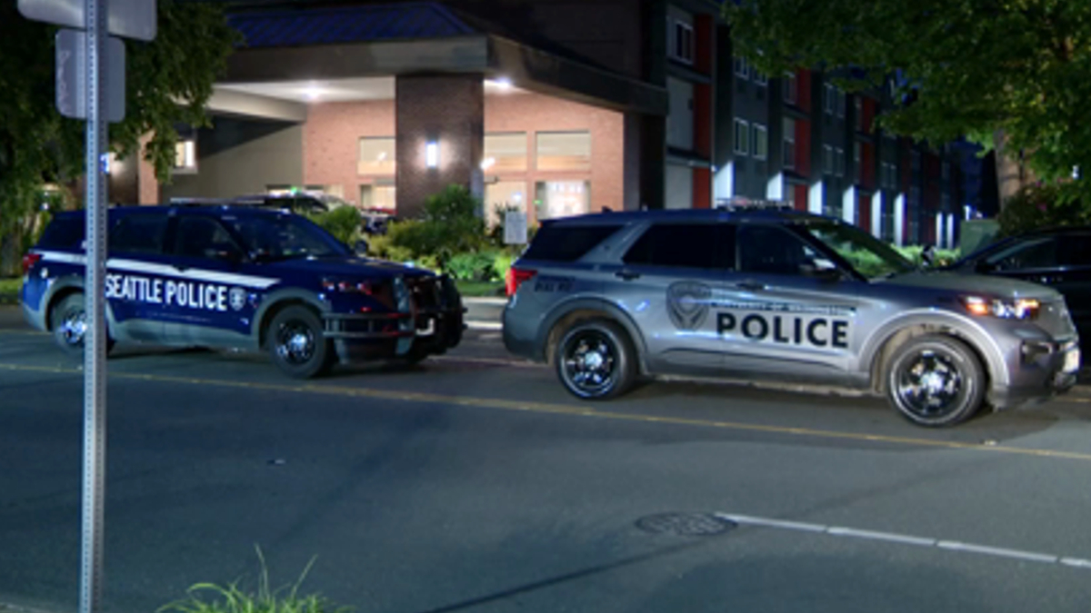 Two police SUVs parked on a city street at night; one shows Seattle Police lettering, the other reads POLICE.