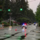 Closed suburban street with road-closure barricades and orange cones; a police car with flashing lights on a wet, reflective road corridor.