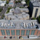 Aerial view of a red-brick office building with large windows and a busy street grid surrounding it, parked cars along the front, and rooftops with HVAC equipment visible.