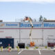 A storefront wall with a large faded sign reading 'Tacoma Discount World' while an orange boom lift works on the roof.