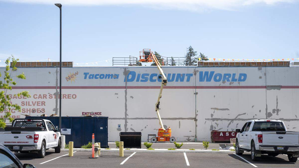 A storefront wall with a large faded sign reading 'Tacoma Discount World' while an orange boom lift works on the roof.